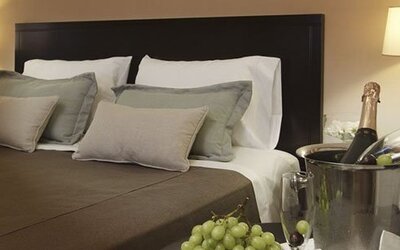 Close view of a king bed with layered pillows, dark headboard, bedside lamps, and champagne at El Conquistador Hotel.