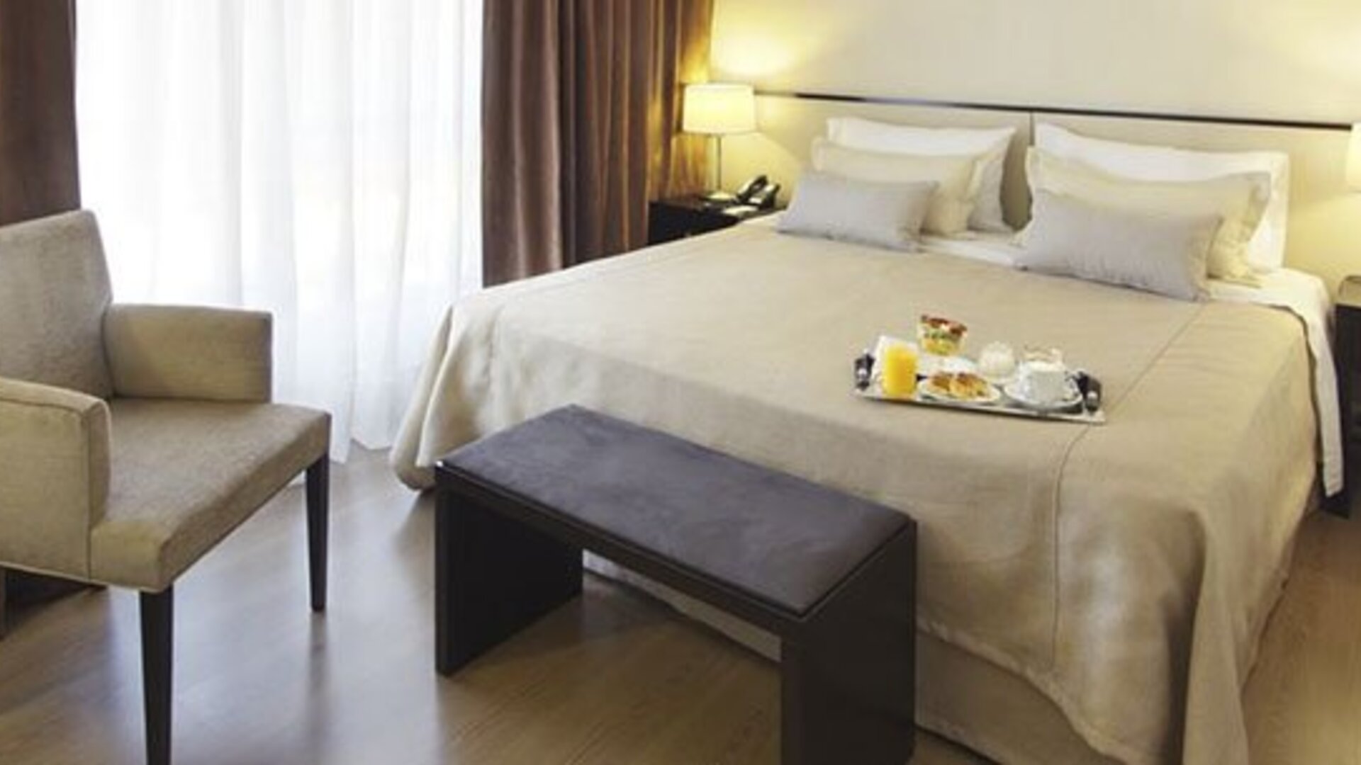Guest room with a king bed, armchair, bench, bedside tables, lamps, and breakfast tray at El Conquistador Hotel.