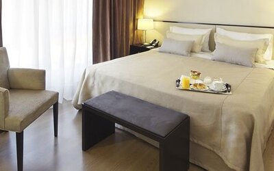 Guest room with a king bed, armchair, bench, bedside tables, lamps, and breakfast tray at El Conquistador Hotel.