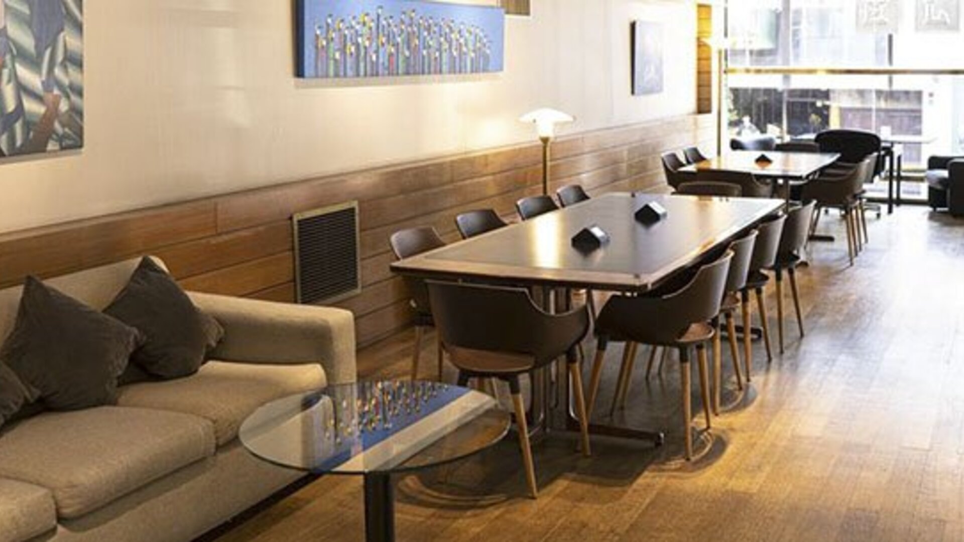 Lounge and dining area with a long table, chairs, sofa, artwork, and windows overlooking the street at El Conquistador Hotel.