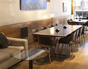 Lounge and dining area with a long table, chairs, sofa, artwork, and windows overlooking the street at El Conquistador Hotel.