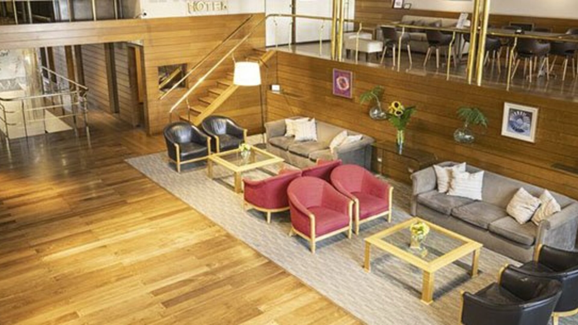 Hotel lounge with wood flooring, red and gray armchairs, sofas, coffee tables, and framed artwork at El Conquistador Hotel