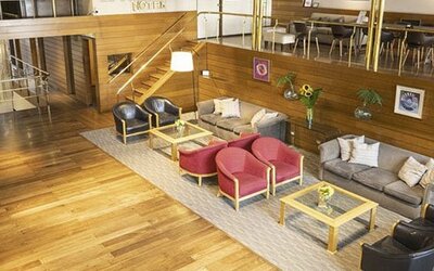 Hotel lounge with wood flooring, red and gray armchairs, sofas, coffee tables, and framed artwork at El Conquistador Hotel
