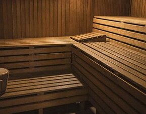 Wood-paneled sauna with tiered benches, a heater, and bucket inside at El Conquistador Hotel.