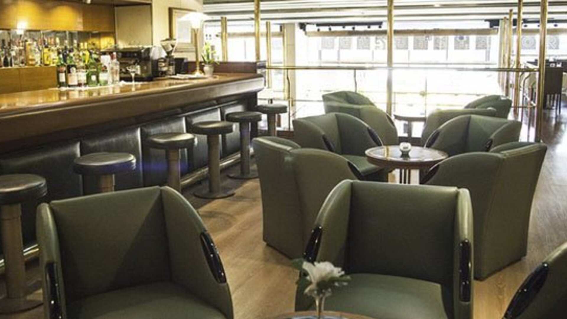 Hotel bar and lounge with green armchairs, round tables, bar stools, and large windows at El Conquistador Hotel.