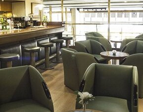Hotel bar and lounge with green armchairs, round tables, bar stools, and large windows at El Conquistador Hotel.