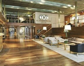 Spacious hotel lobby with a curved reception desk, wood flooring, lounge seating, and mezzanine at El Conquistador Hotel.