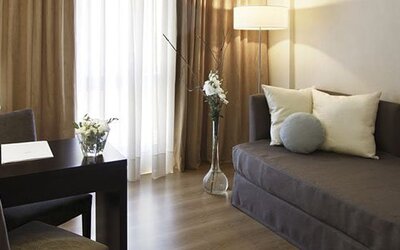 Guest room with a single sofa bed, desk and chair, floor lamp, and curtains beside a bright window at El Conquistador Hotel.