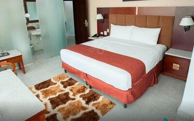 Guest room with a king bed, red runner, padded headboard, bedside tables, and patterned rug at Hotel Grand International.