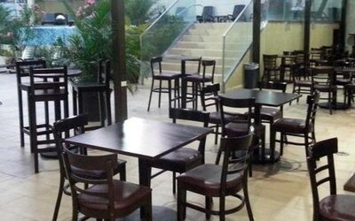 Indoor dining area with dark wooden tables and chairs beside large windows overlooking an outdoor pool at Hotel Grand International.