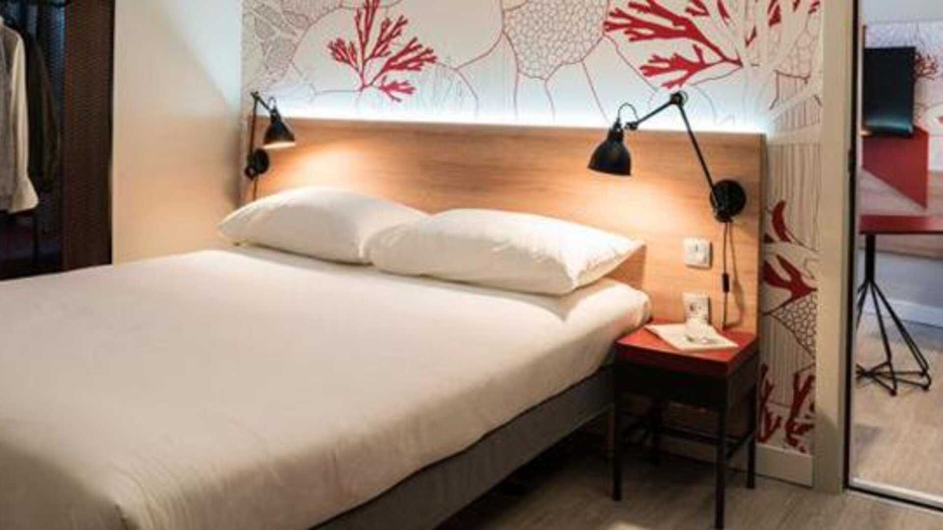 Guest room with a double bed, coral-patterned wall, bedside table, wardrobe, and mirrored closet at Hotel ibis Styles Barcelona City Bogatell.