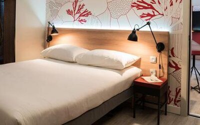 Guest room with a double bed, coral-patterned wall, bedside table, wardrobe, and mirrored closet at Hotel ibis Styles Barcelona City Bogatell.