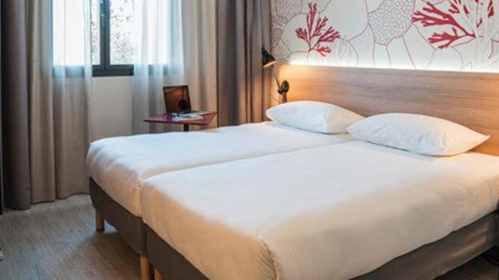 Guest room with a double bed, wooden headboard, coral-patterned wall, bedside lamps, and curtained window at Hotel ibis Styles Barcelona City Bogatell.