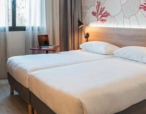 Guest room with a double bed, wooden headboard, coral-patterned wall, bedside lamps, and curtained window at Hotel ibis Styles Barcelona City Bogatell.