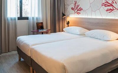 Guest room with a double bed, wooden headboard, coral-patterned wall, bedside lamps, and curtained window at Hotel ibis Styles Barcelona City Bogatell.