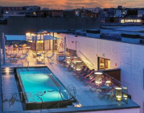 Rooftop swimming pool surrounded by lounge chairs, cabanas, and outdoor seating at Hotel ibis Styles Barcelona City Bogatell.