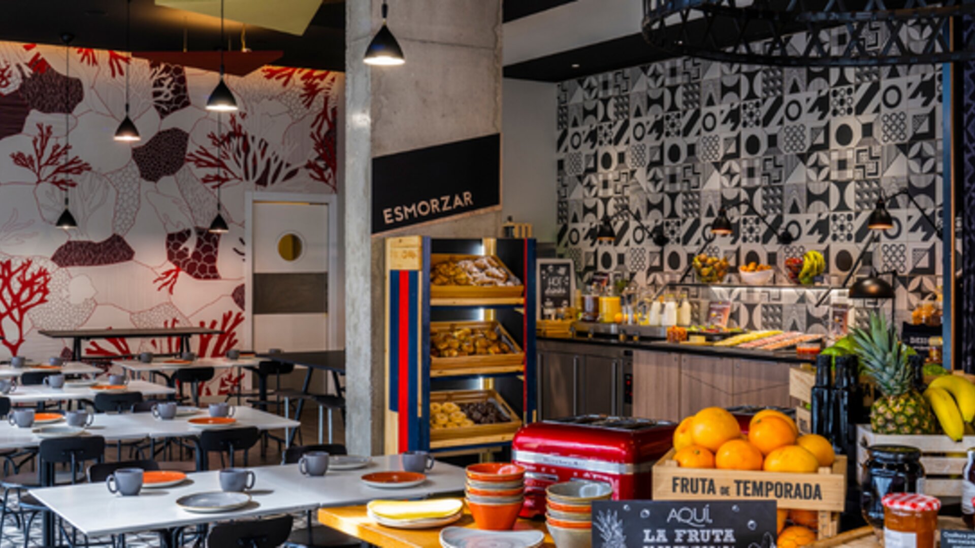 Breakfast buffet with pastries, fruit, cold foods, and drinks beside a patterned dining area at Hotel ibis Styles Barcelona City Bogatell.