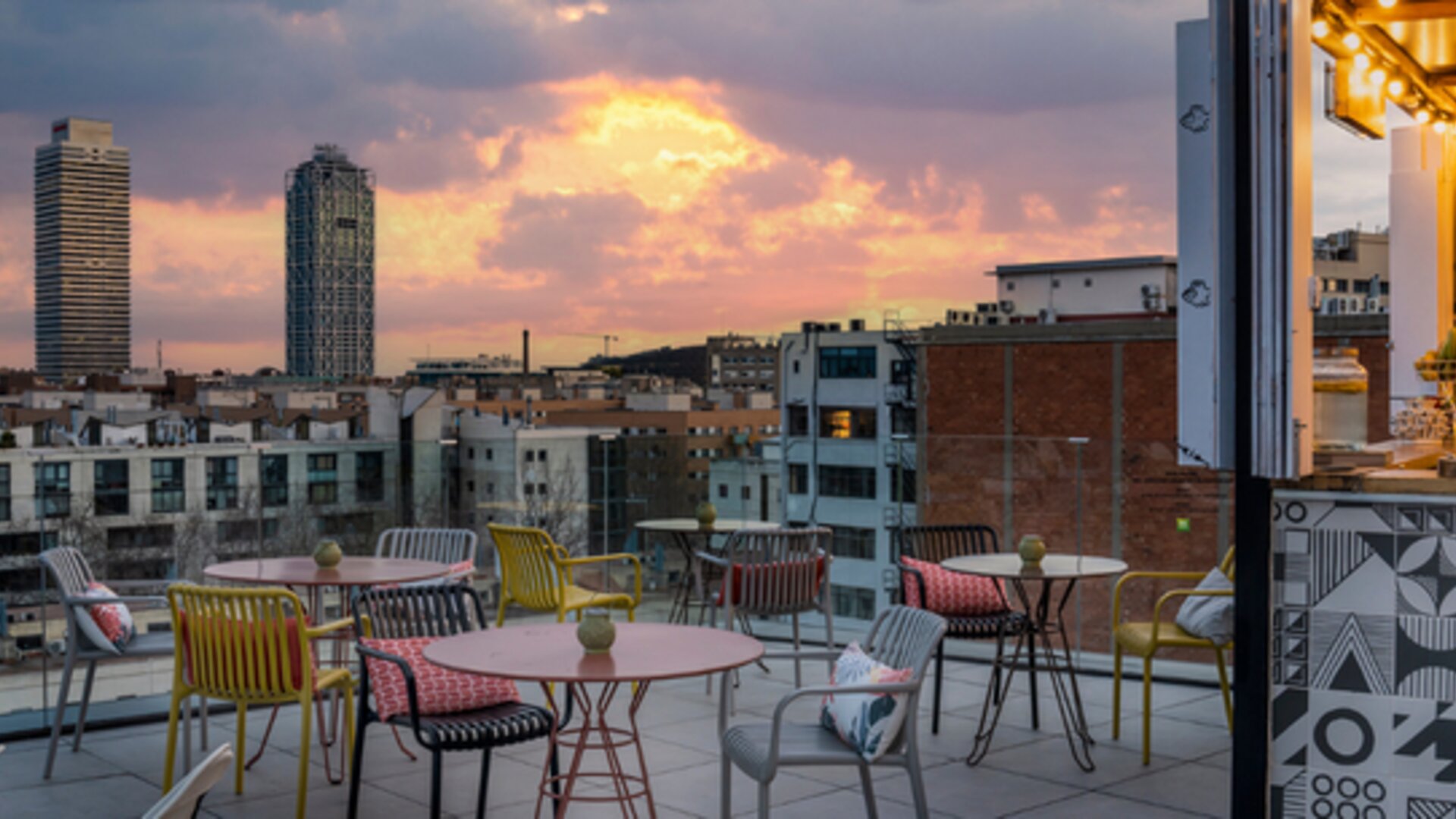 Rooftop terrace with colorful chairs, round tables, lounge seating, and city views at Hotel ibis Styles Barcelona City Bogatell.