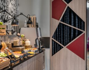 Breakfast buffet with pastries, fruit, drinks, and food displays beneath black pendant lamps at Hotel ibis Styles Barcelona City Bogatell.