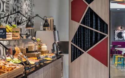 Breakfast buffet with pastries, fruit, drinks, and food displays beneath black pendant lamps at Hotel ibis Styles Barcelona City Bogatell.