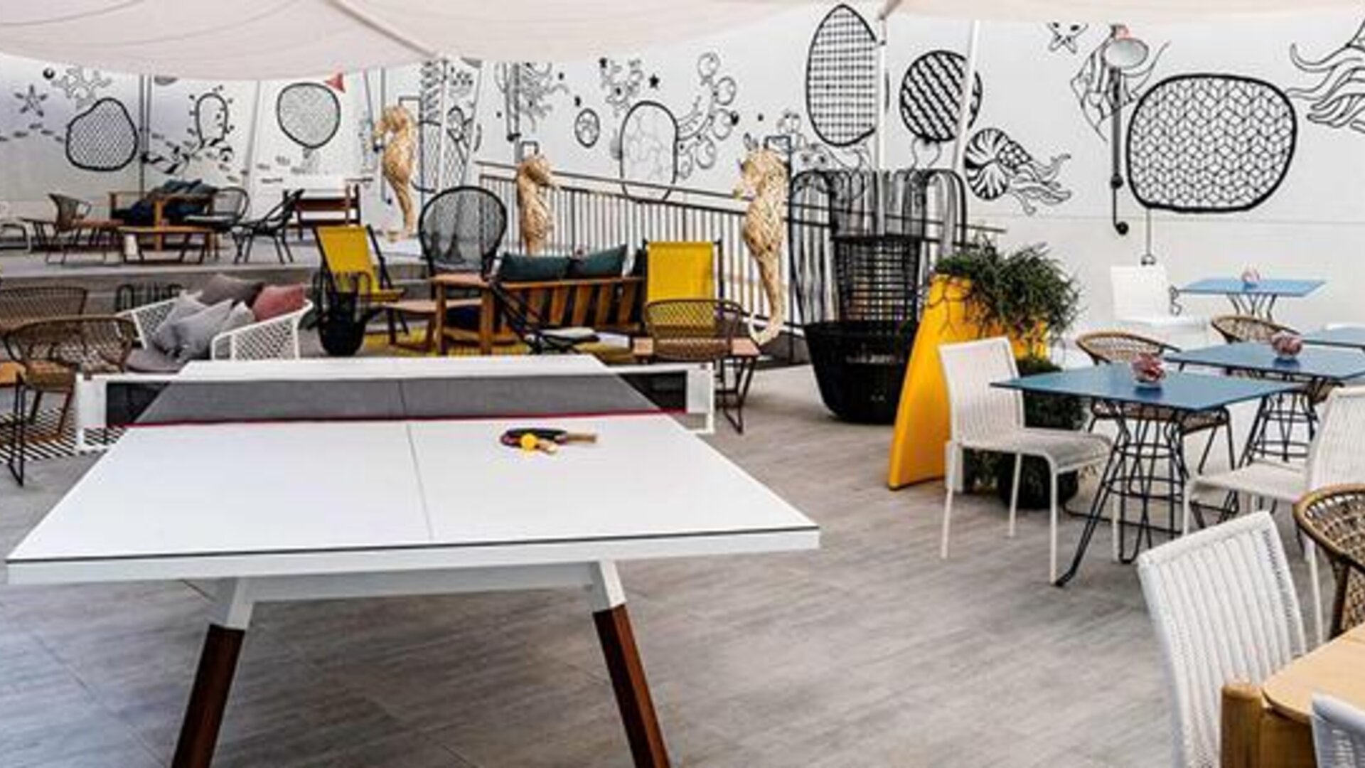 Leisure area with a table tennis table, colorful chairs, tables, and illustrated wall murals at Hotel ibis Styles Barcelona City Bogatell.