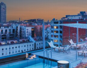 Rooftop terrace with swimming pool, lounge chairs, city skyline, and outdoor seating at Hotel ibis Styles Barcelona City Bogatell.