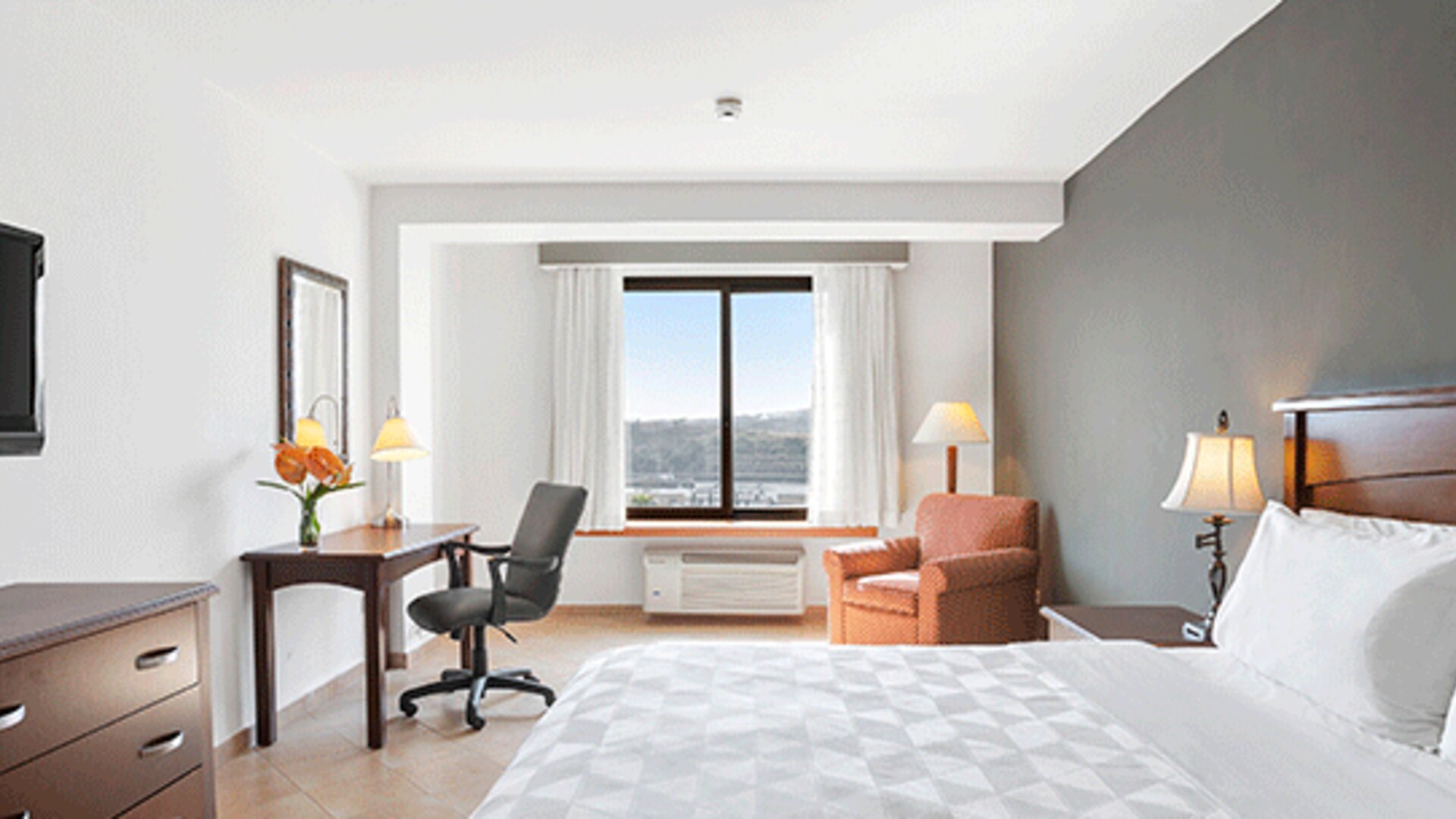 Guest room with a king bed, desk, office chair, armchair, television and large window overlooking the landscape at Holiday Inn Panama Canal.