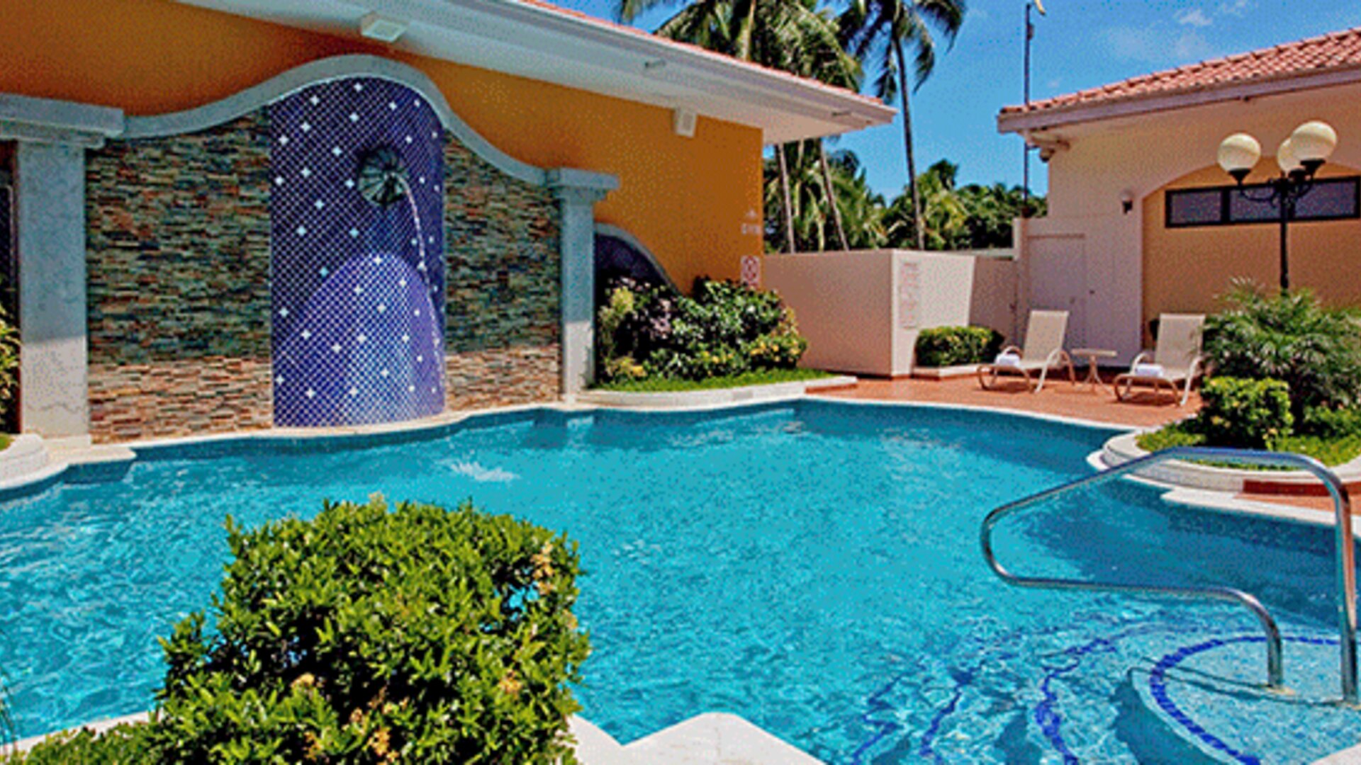 Outdoor swimming pool surrounded by lounge chairs, tropical landscaping and a tiled waterfall feature at Holiday Inn Panama Canal.