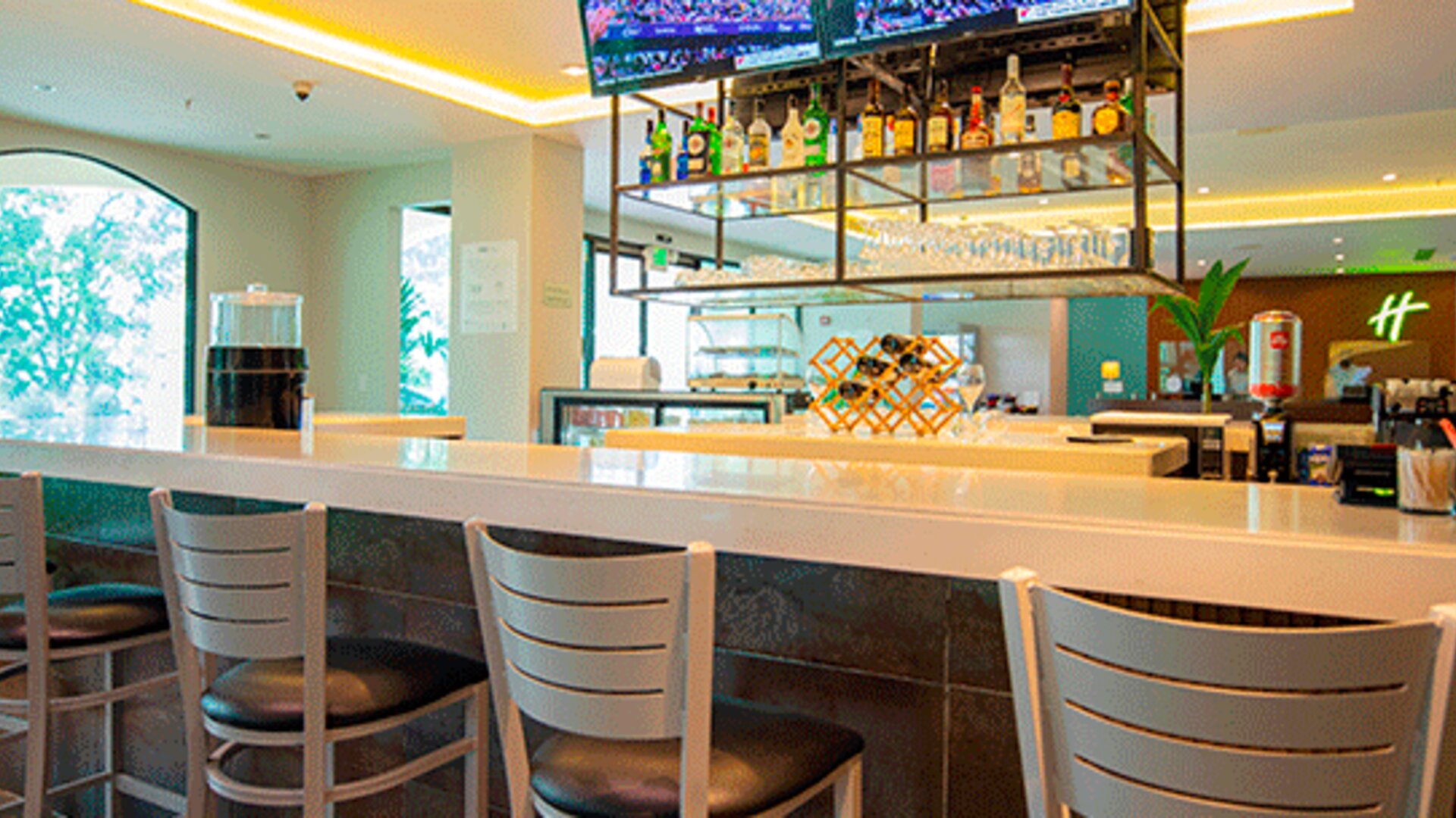 Hotel bar with a white counter, high stools, liquor display and televisions at Holiday Inn Panama Canal.