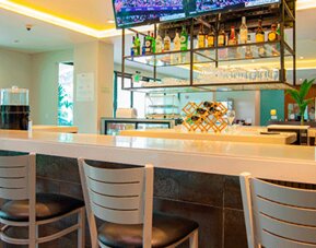 Hotel bar with a white counter, high stools, liquor display and televisions at Holiday Inn Panama Canal.