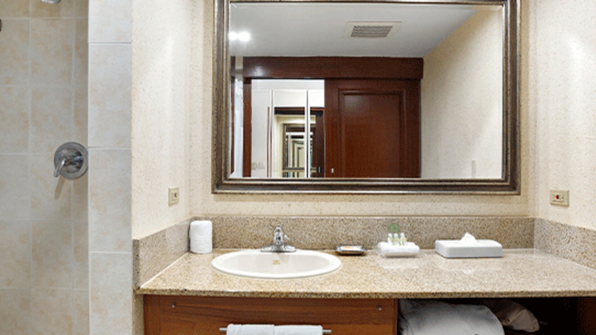 Hotel bathroom with a granite vanity, sink, large mirror and tiled shower at Holiday Inn Panama Canal.