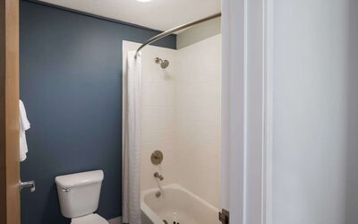 Bathroom with a bathtub, shower, toilet, and dark blue accent wall at Best Western Plus Mountain View Auburn Inn.