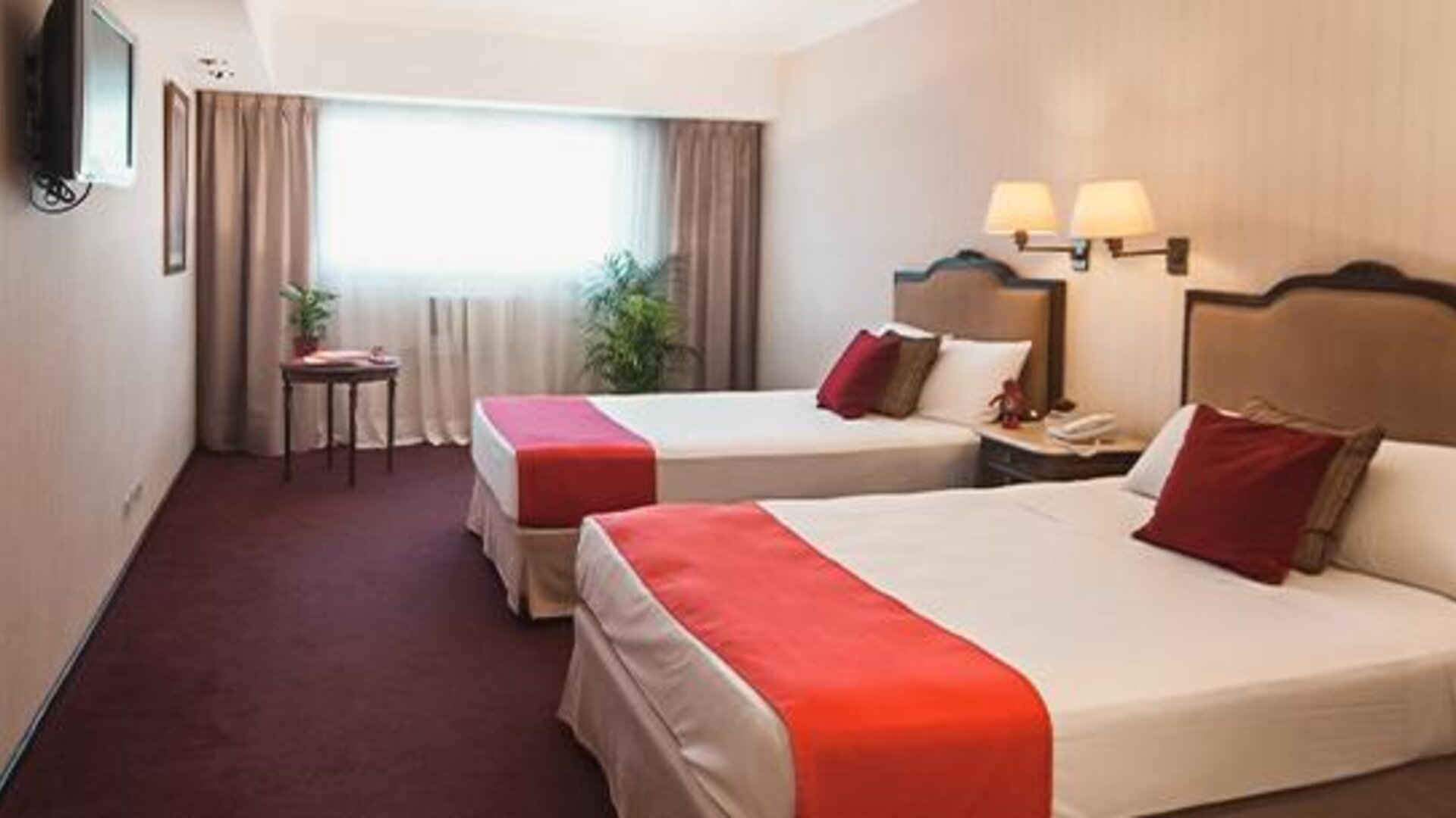 Guest room with two twin beds, white linens, red bed runners, red accent pillows and a large window at Ramada by Wyndham Buenos Aires Centro.