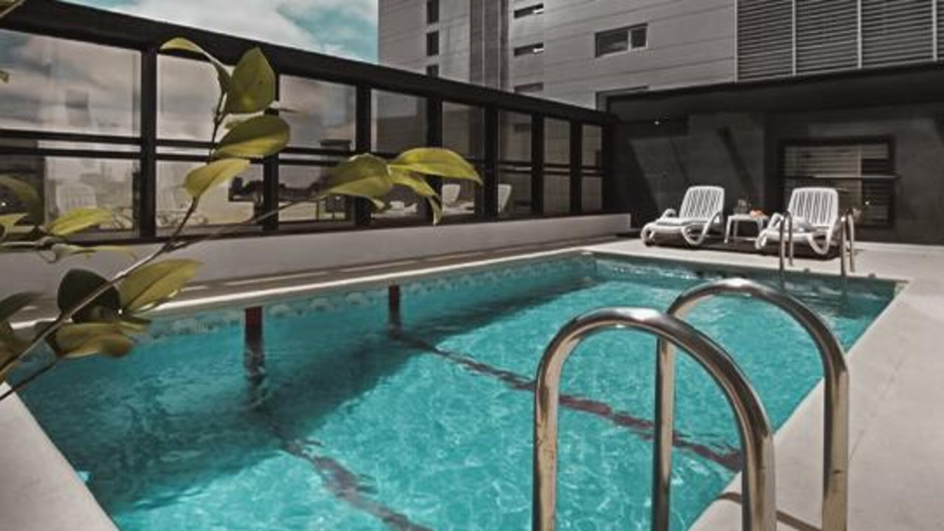 Outdoor swimming pool with turquoise water, metal handrails and white lounge chairs at Ramada by Wyndham Buenos Aires Centro.