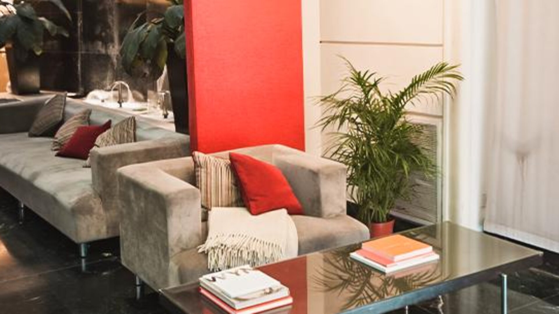 Hotel seating area with gray armchairs and sofas, red cushions, plants and a glass coffee table at Ramada by Wyndham Buenos Aires Centro.