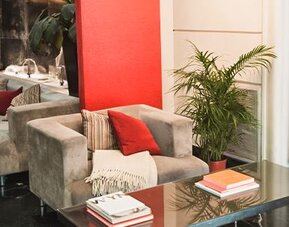 Hotel seating area with gray armchairs and sofas, red cushions, plants and a glass coffee table at Ramada by Wyndham Buenos Aires Centro.
