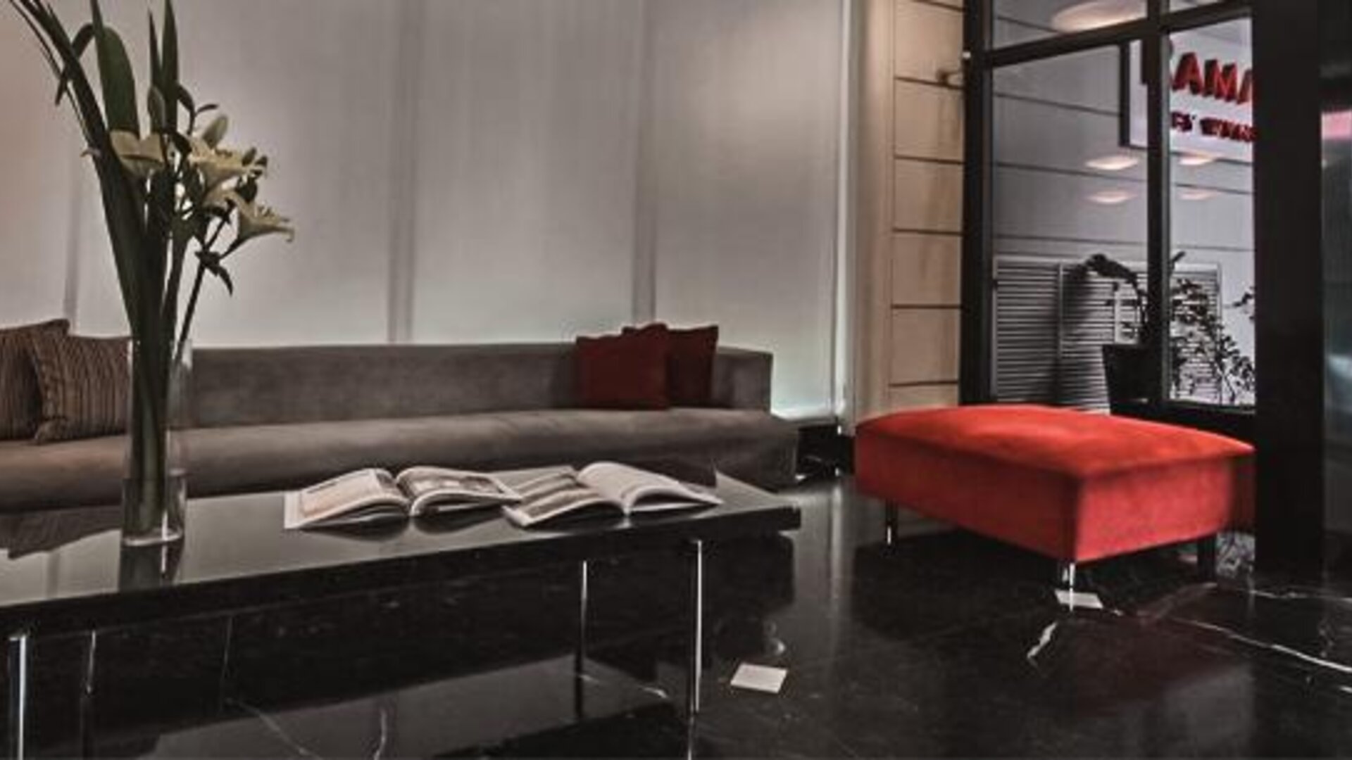 Hotel lounge with a gray sofa, red ottoman, marble coffee table and open books at Ramada by Wyndham Buenos Aires Centro.