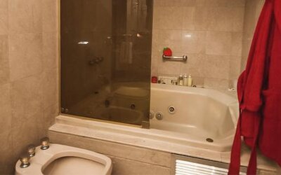 Bathroom with a whirlpool bathtub, glass shower enclosure and red bathrobe at Ramada by Wyndham Buenos Aires Centro.