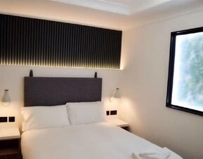 Double guest room with a white bed, dark upholstered headboard, bedside tables, wall-mounted reading lights and a large window at Victoria Inn.
