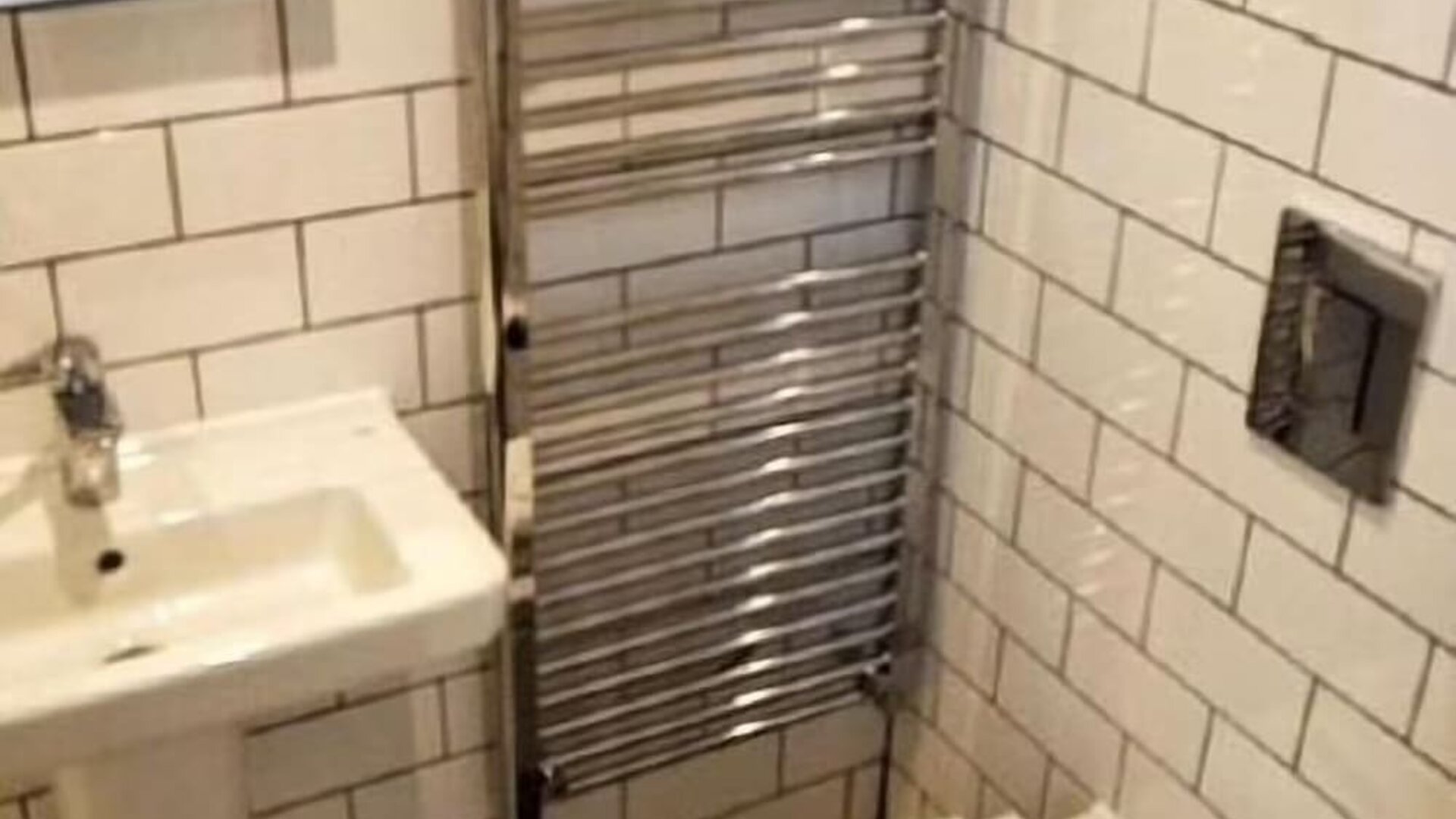 Bathroom with white subway-tile walls, a wall-mounted sink, heated towel rail, toilet and folded white towels at Victoria Inn.