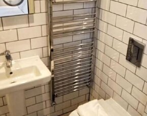 Bathroom with white subway-tile walls, a wall-mounted sink, heated towel rail, toilet and folded white towels at Victoria Inn.