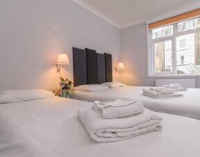 Guest room with two single beds, white linens, folded towels, bedside lamps and a large window at Victoria Inn.