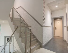 Interior staircase and hallway at Victoria Inn with glass stair railings, gray flooring, white walls and guest room doors.