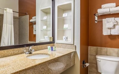 Bathroom with a granite vanity, white sink, large mirror, toiletries, towel rack with folded towels, and toilet at Sleep Inn & Suites Stafford - Sugar Land.
