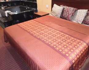 King guest room with a large bed featuring a red and gold patterned bedspread, dark wooden headboard, bedside tables, telephone, and black whirlpool tub beside the bed at Scottish Inn & Suites.