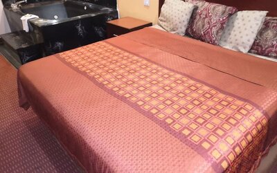 King guest room with a large bed featuring a red and gold patterned bedspread, dark wooden headboard, bedside tables, telephone, and black whirlpool tub beside the bed at Scottish Inn & Suites.