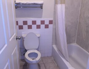 Bathroom with a bathtub and shower curtain, toilet, towel rack with folded towels, grab bar, and tiled walls at Scottish Inn & Suites.