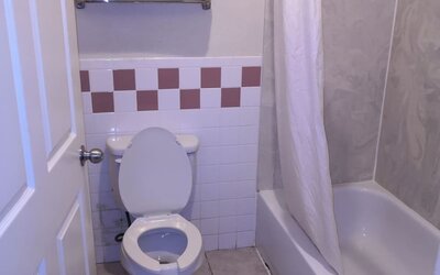 Bathroom with a bathtub and shower curtain, toilet, towel rack with folded towels, grab bar, and tiled walls at Scottish Inn & Suites.