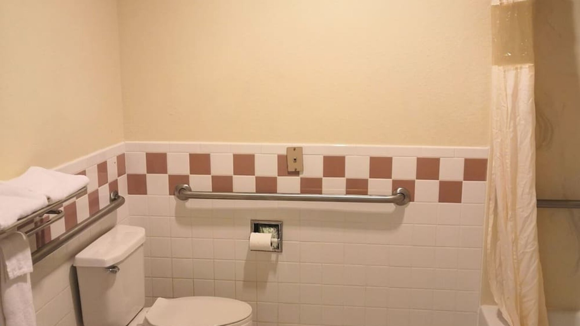 Accessible bathroom with a toilet, bathtub and shower, grab bars, towel racks, and tiled walls at Scottish Inn & Suites.