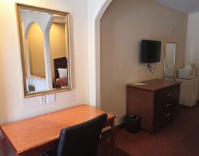 Guest room workspace with a wooden desk and chair, wall mirror, television, dresser, microwave, and mini refrigerator at Scottish Inn & Suites.
